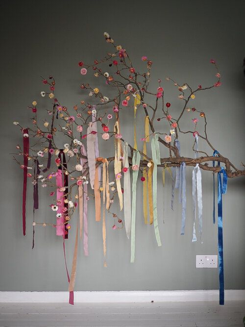 an art piece with ribbons hanging from it's branches and flowers on the wall