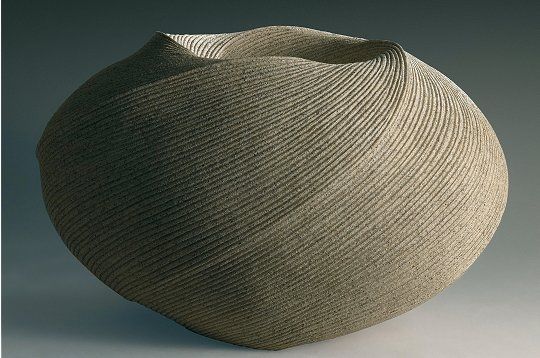 a large round vase sitting on top of a table next to a white wall and floor