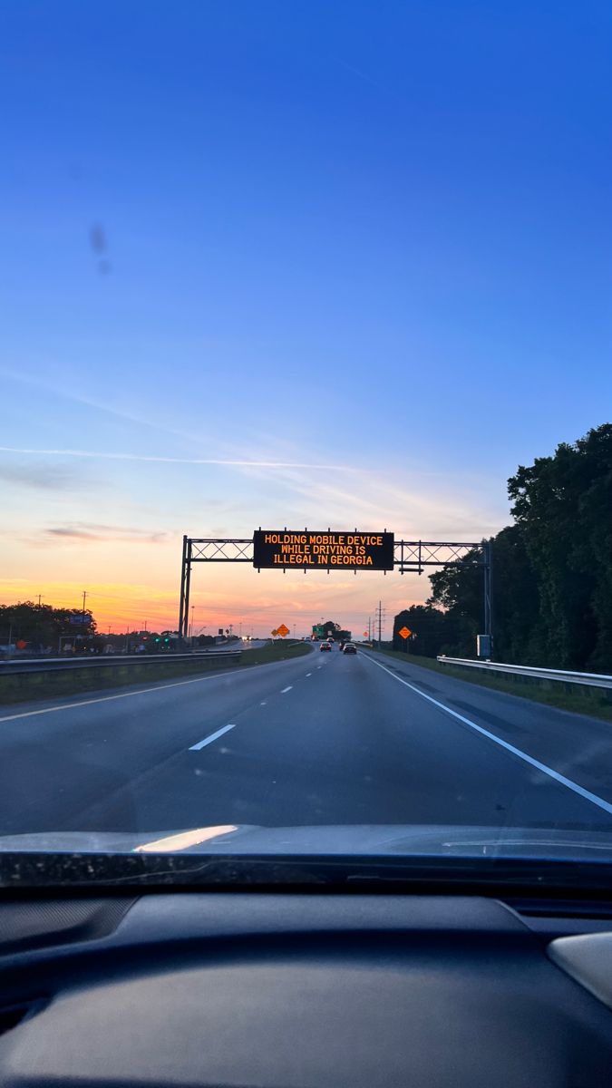 the sun is setting on an empty highway with traffic lights and street signs above it