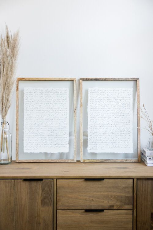 two framed pictures sitting on top of a wooden dresser next to a vase filled with dry grass