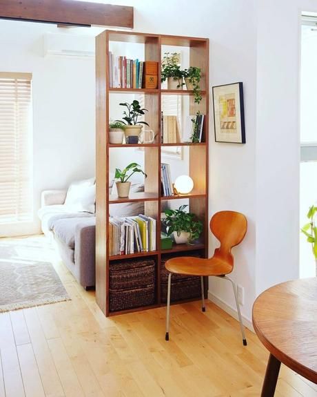 a living room filled with furniture and a book shelf next to a window on top of a hard wood floor