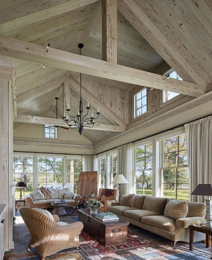 a living room filled with lots of furniture next to large windows and wooden beams on the ceiling