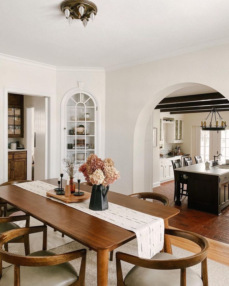 a dining room table with chairs and a vase filled with flowers sitting on top of it