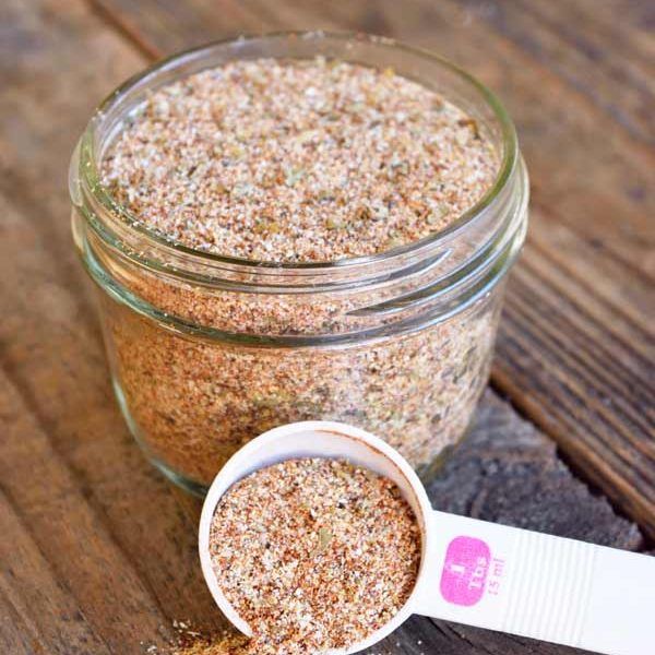 a glass jar filled with lots of different types of seasoning on top of a wooden table