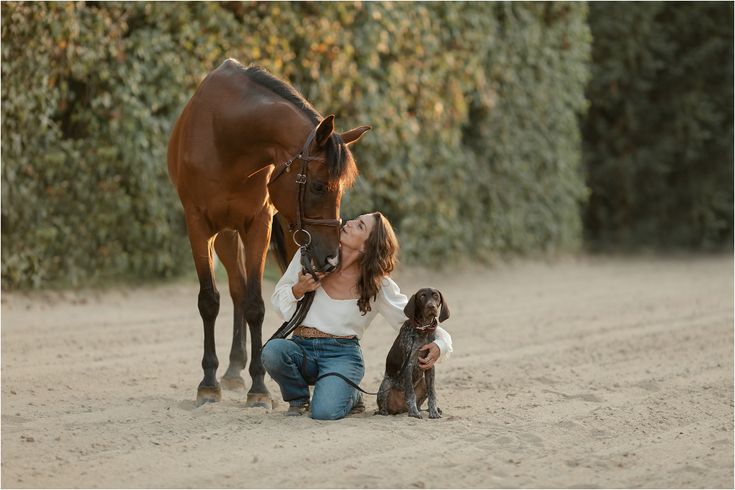 a woman kneeling down next to a brown horse