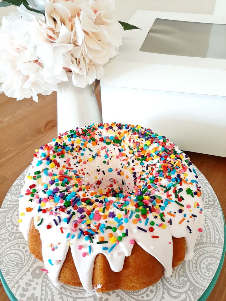 a cake with white frosting and sprinkles sits on a plate next to flowers