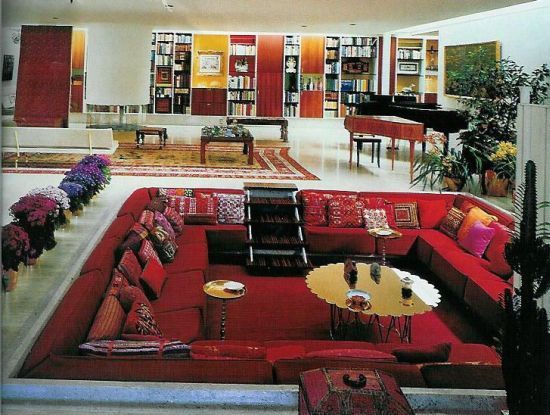 a living room filled with red couches and lots of bookshelves next to a piano