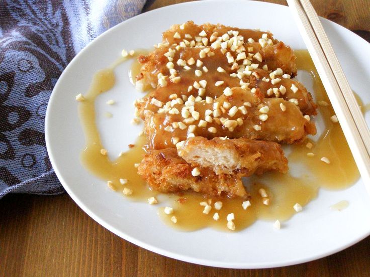 a white plate topped with meat covered in sauce and sesame seeds next to chopsticks