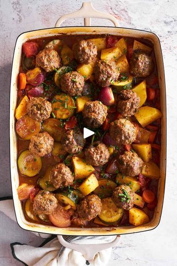 meatballs and vegetables in a casserole dish on top of a white table