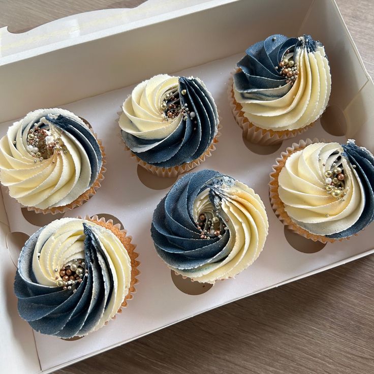 six cupcakes with blue and white frosting in a box on a table