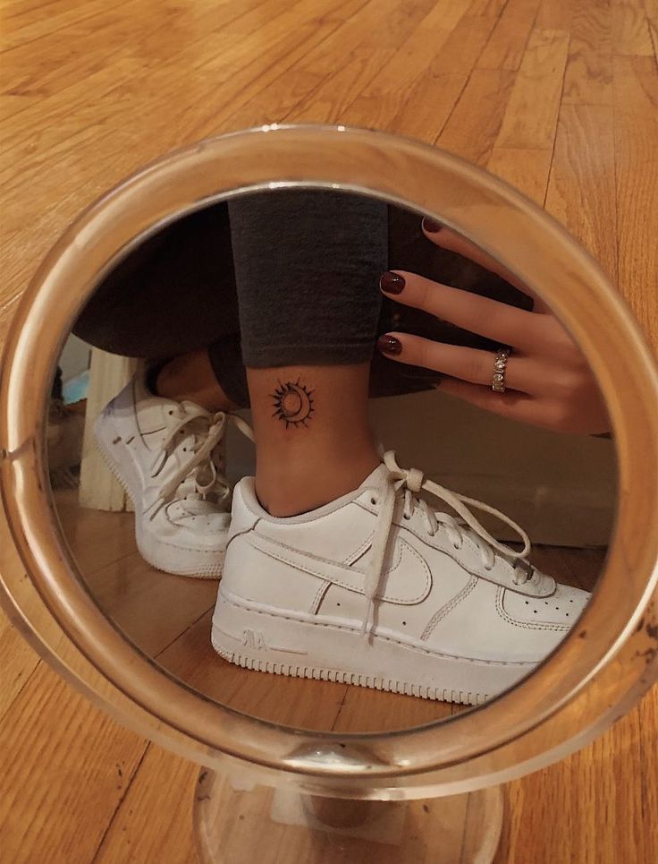 a woman's foot with a small tattoo on her left ankle in front of a mirror