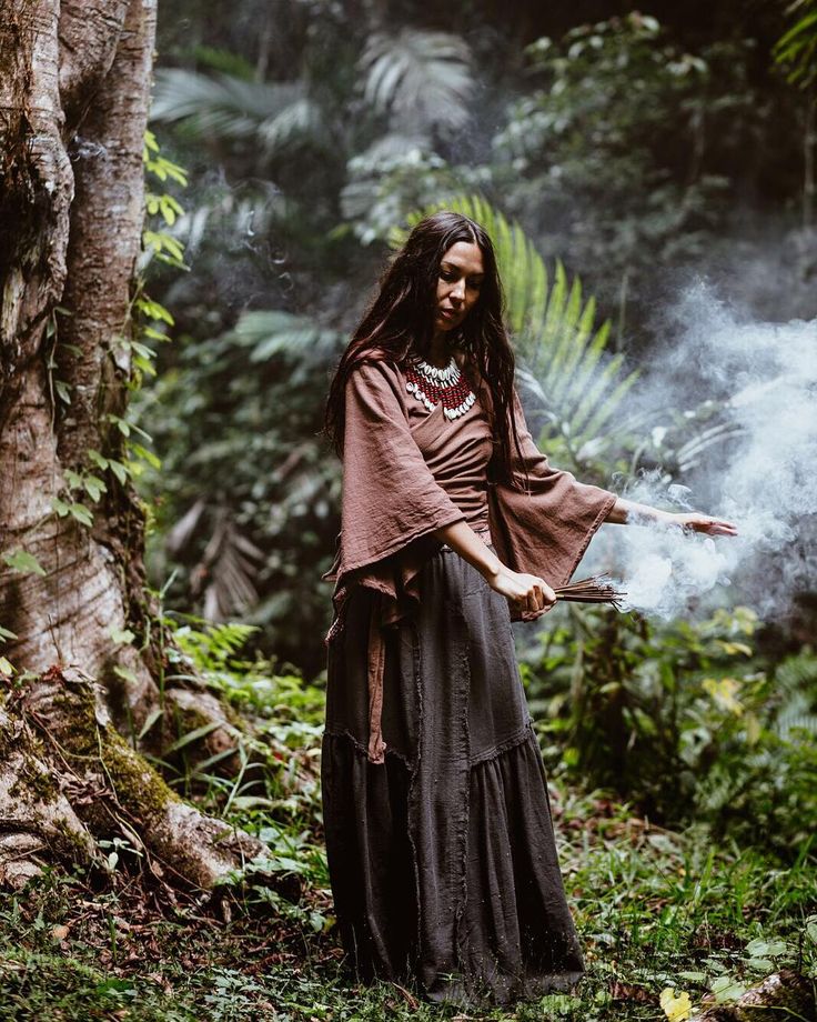 a man with dreadlocks standing in front of a tree and holding a stick