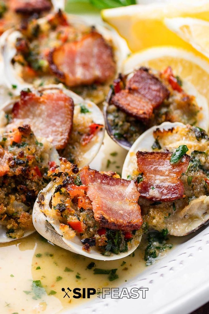 clams with bacon and spinach on a white plate next to lemon wedges