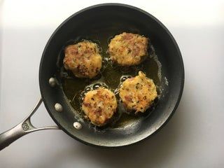 four fried meat patties in a frying pan on a stove top with a spatula