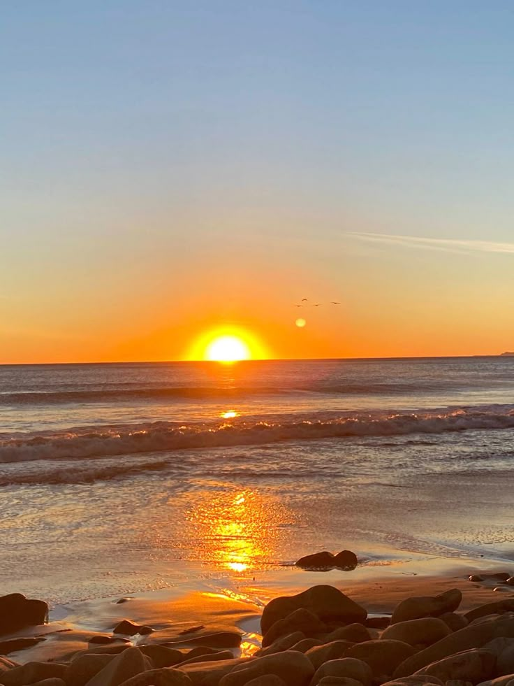 the sun is setting over the ocean with rocks