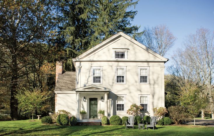 a large white house sitting in the middle of a lush green field next to trees