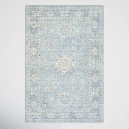 a light blue rug with an ornate design on the top and bottom, in front of a white wall