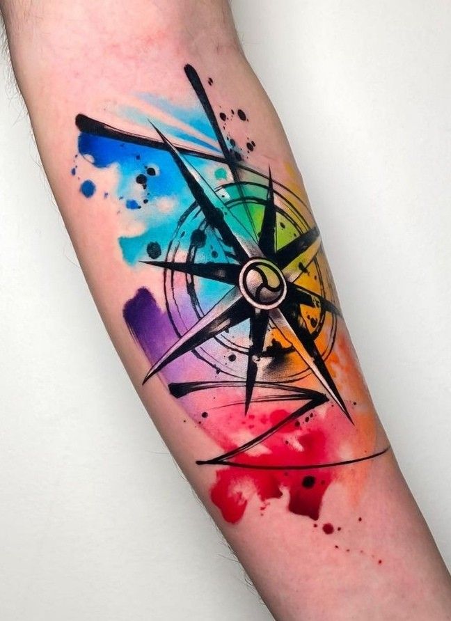 a colorful compass tattoo on the left forearm and arm with watercolor paint splatters