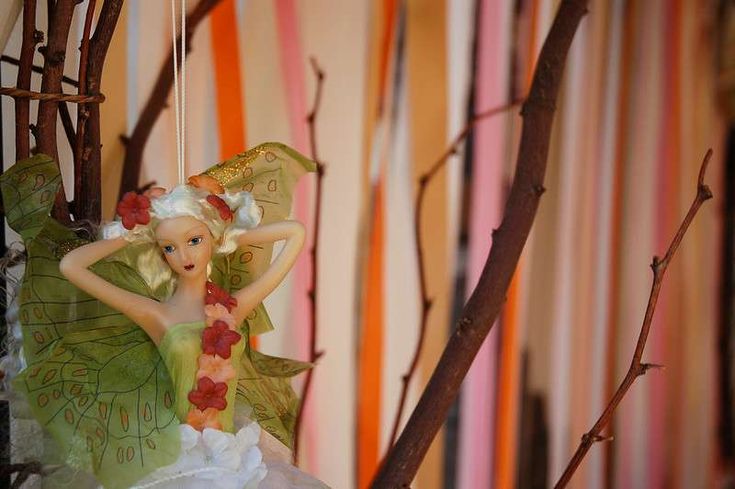 a fairy figurine hanging from a tree branch in front of a striped wall