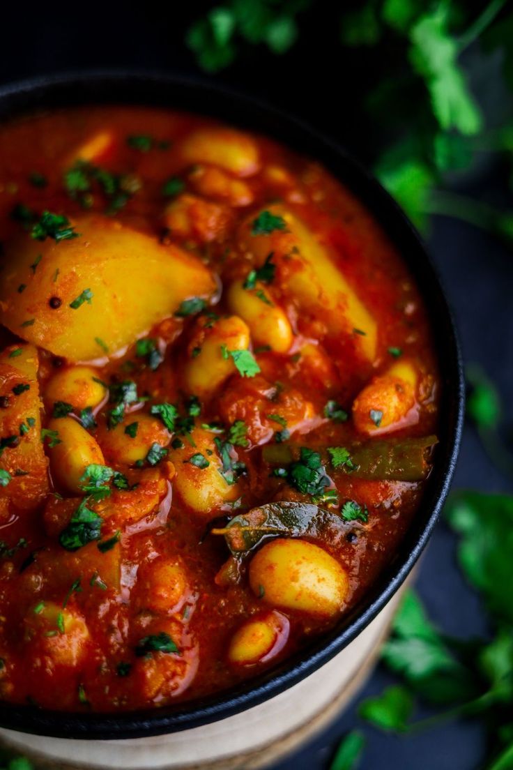 a close up of a bowl of stew with potatoes and herbs on the side, surrounded by parsley