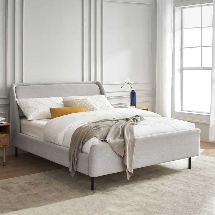 a white bed sitting in a bedroom on top of a hard wood floor next to a window