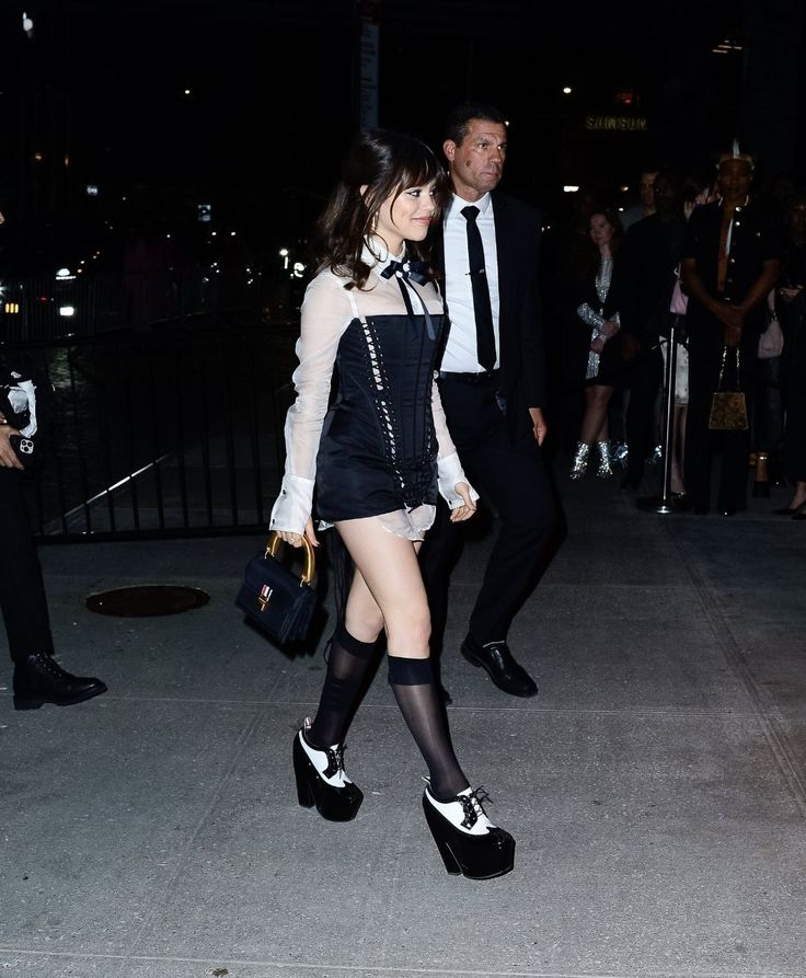 a woman in short skirt and high heels walking down the street at night with other people behind her