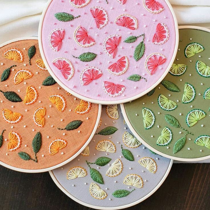 four different colored embroidery designs on small hoops with green leaves and orange slices in the center