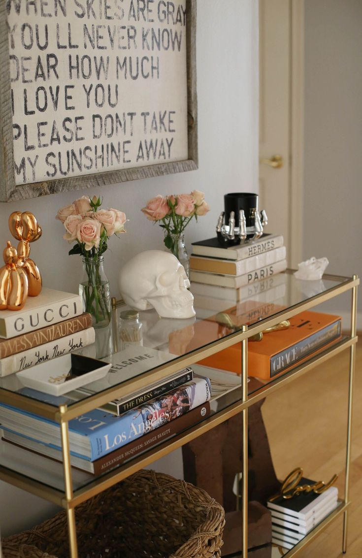 a glass table topped with books and vases filled with flowers next to a painting