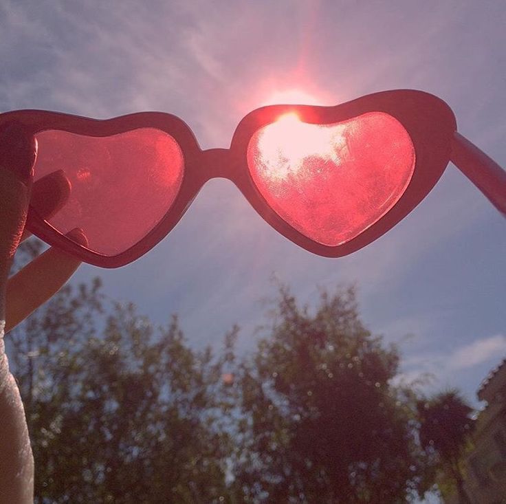 someone holding up two heart shaped sunglasses in front of the sun with trees behind them