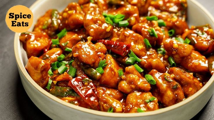 a white bowl filled with chicken covered in sauce and garnished with green onions