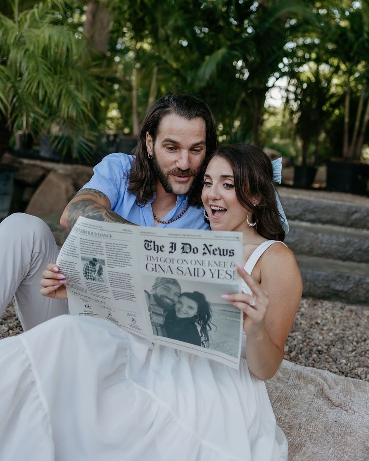 a man and woman sitting next to each other on the ground reading a news paper