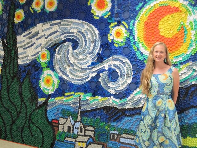 a woman standing in front of a mosaic wall with a painting on it's side