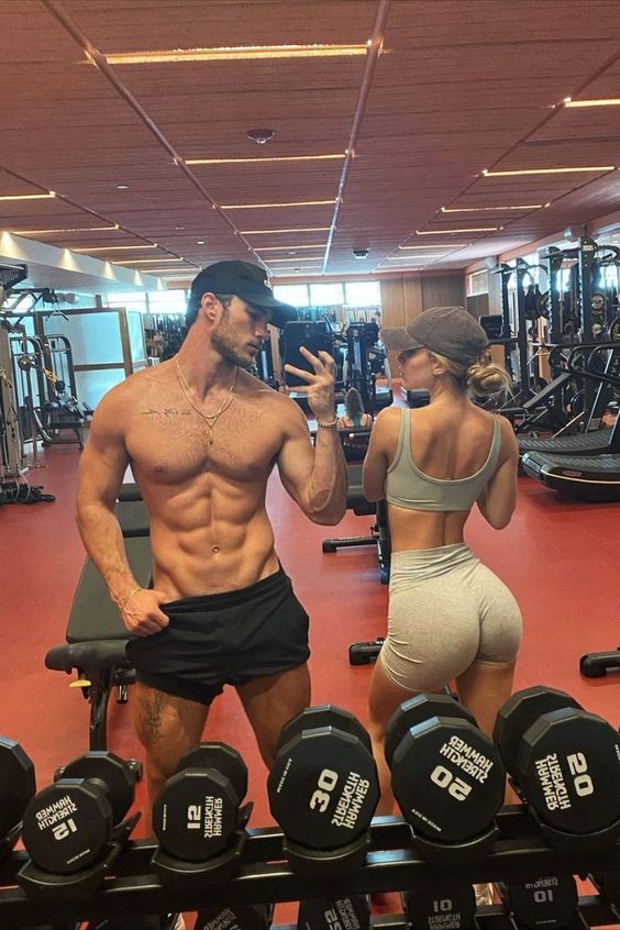 a man and woman standing next to each other in front of dumbs at the gym