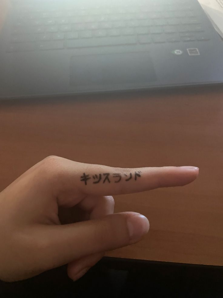 a person's finger with writing on it and a laptop in the back ground