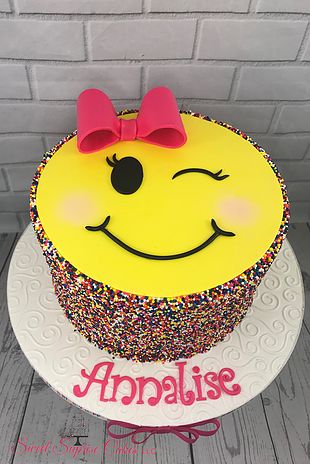 a smiley face cake with sprinkles and a pink bow on the top