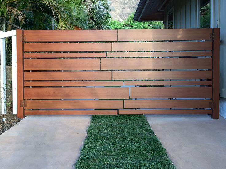 a wooden fence in front of a house with grass on the ground and trees behind it