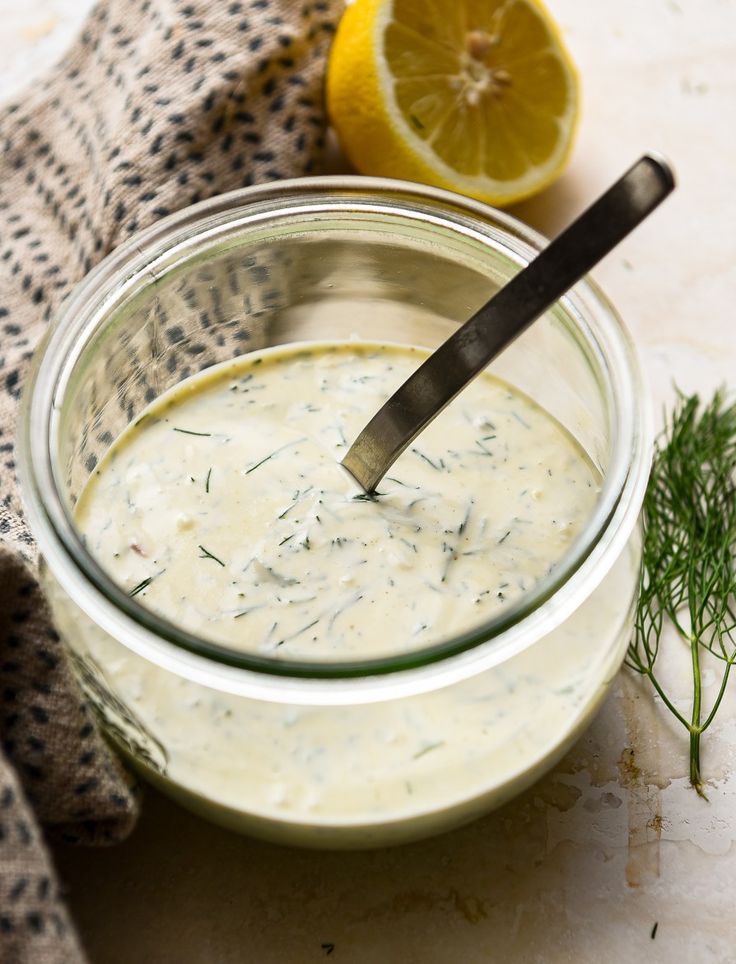 a glass bowl filled with white sauce next to a lemon slice