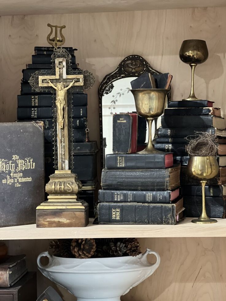 a shelf filled with books and candles next to a cross on top of a table