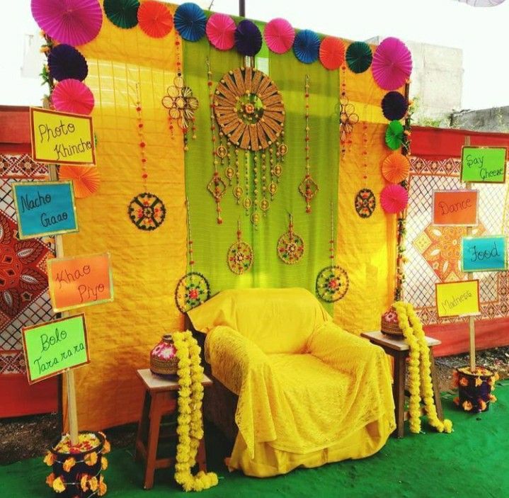 a yellow chair sitting in front of a green wall covered in paper flowers and pom poms