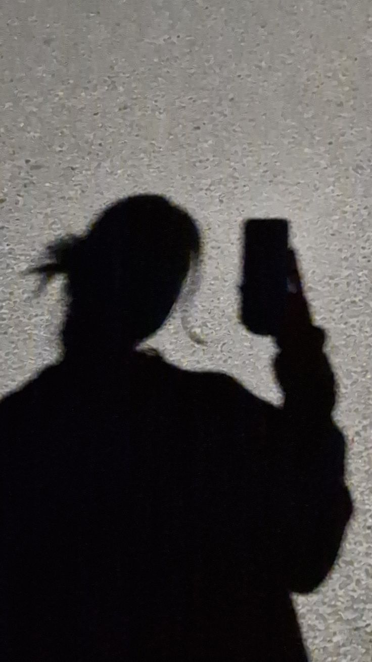 a shadow of a person holding a cell phone in their hand and looking at it