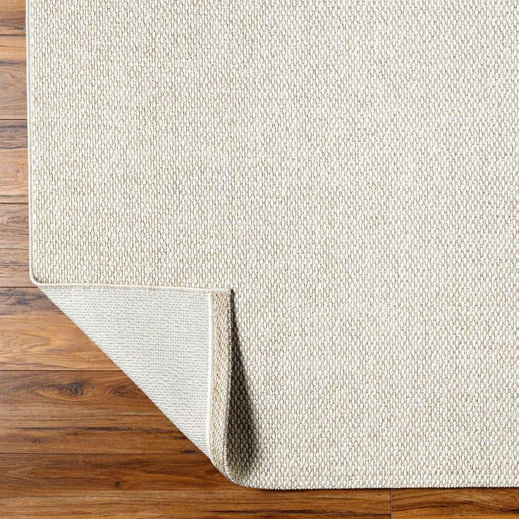 a white rug on top of a wooden floor with a wood flooring board in the background