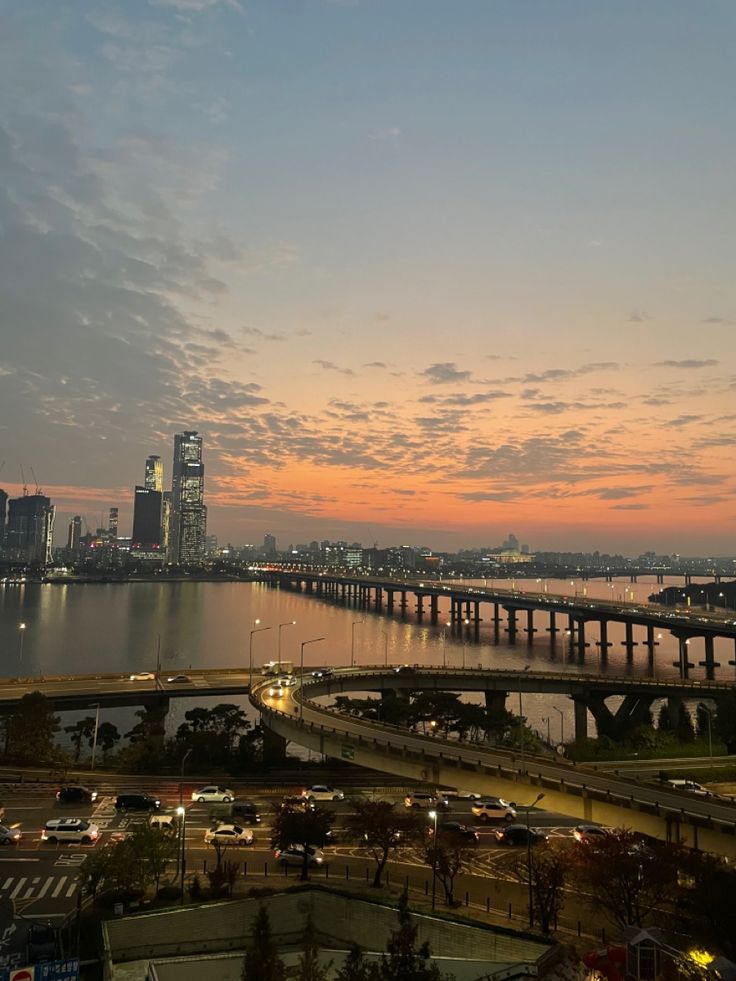 the city skyline is lit up at night with cars driving on the road and bridge in the background