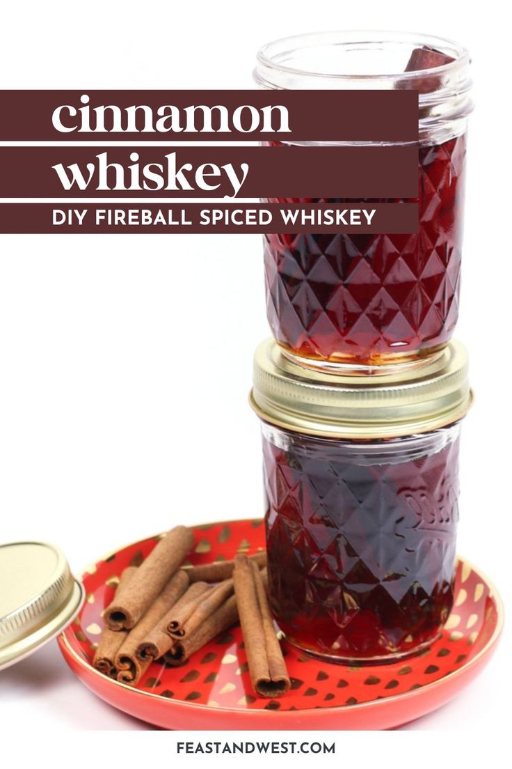 cinnamon whiskey is in a glass jar on a red plate with cinnamon sticks and spices