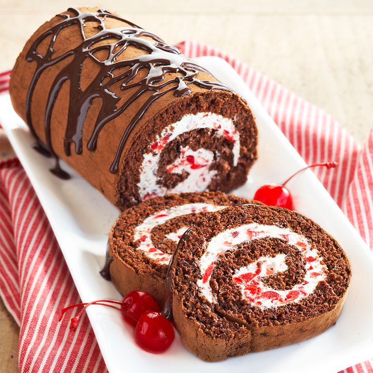 a chocolate roll with cream filling and cherries on a white plate next to a cherry