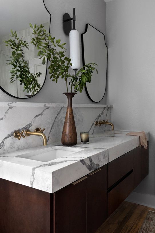 a bathroom with marble counter tops and two mirrors on the wall above it is a plant in a vase