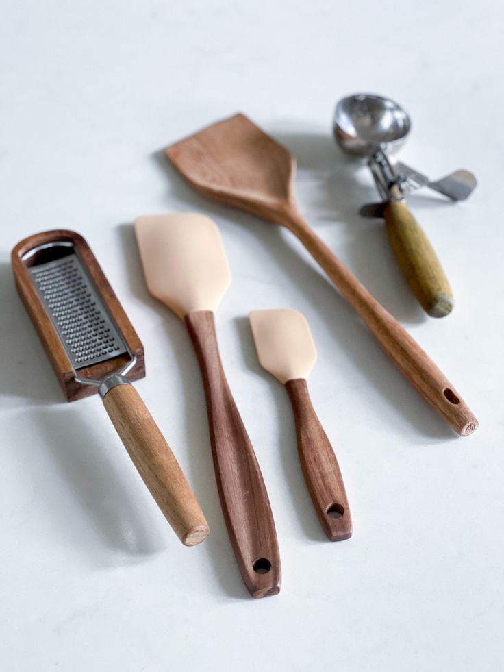 three wooden utensils and two graters on a white counter top with spoons