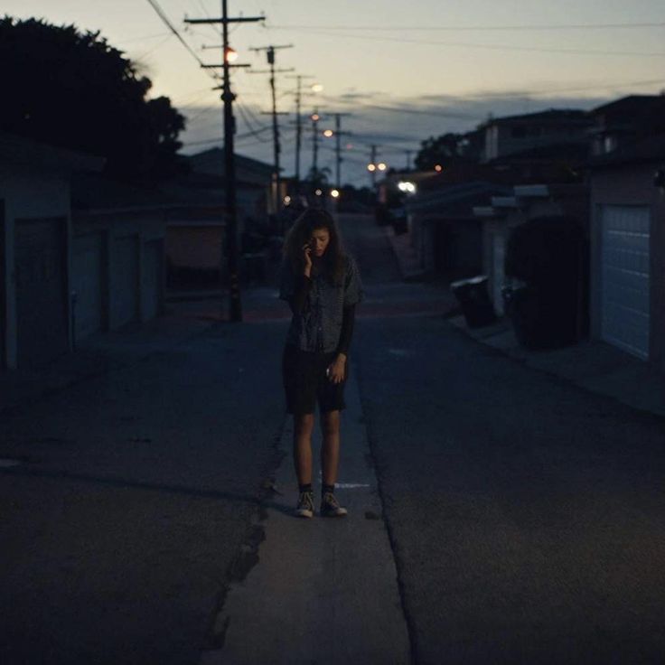 a woman standing on the side of a road talking on a cell phone at night