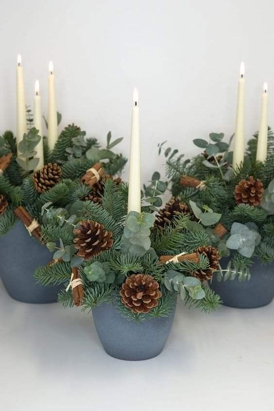 candles are lit in small blue pots with greenery and pine cones