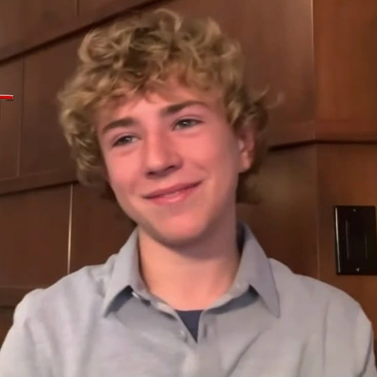 a young man with blonde hair is smiling at the camera while wearing a gray shirt