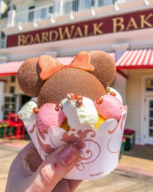 someone holding up a cupcake with mickey ears on it in front of a building